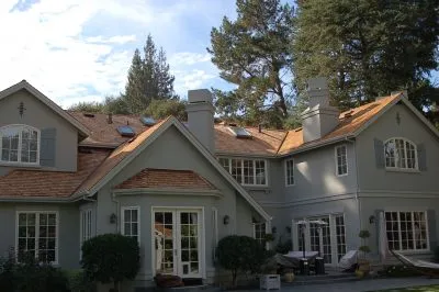 A large gray house with a new roof, completed by Mid-Peninsula Roofing Inc. in Burlingame, surrounded by trees.